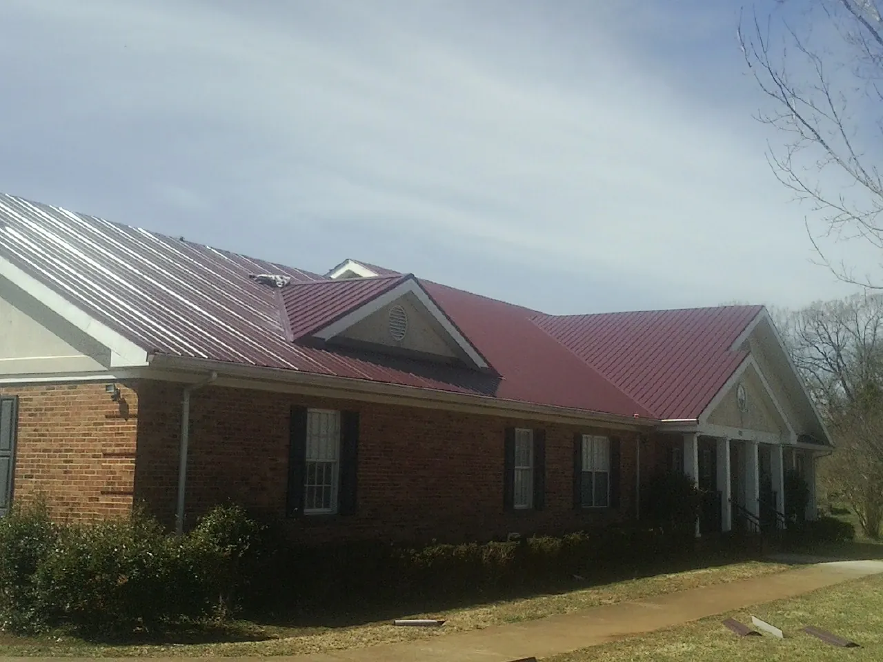 Red metal roof with gabled entries on a long brick building, from a Hail Damage Roof Repair job in Athol