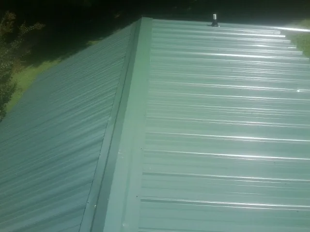 New green metal panels meeting at the ridge of a roof — Flat Roof Repair work by our crew in Athol