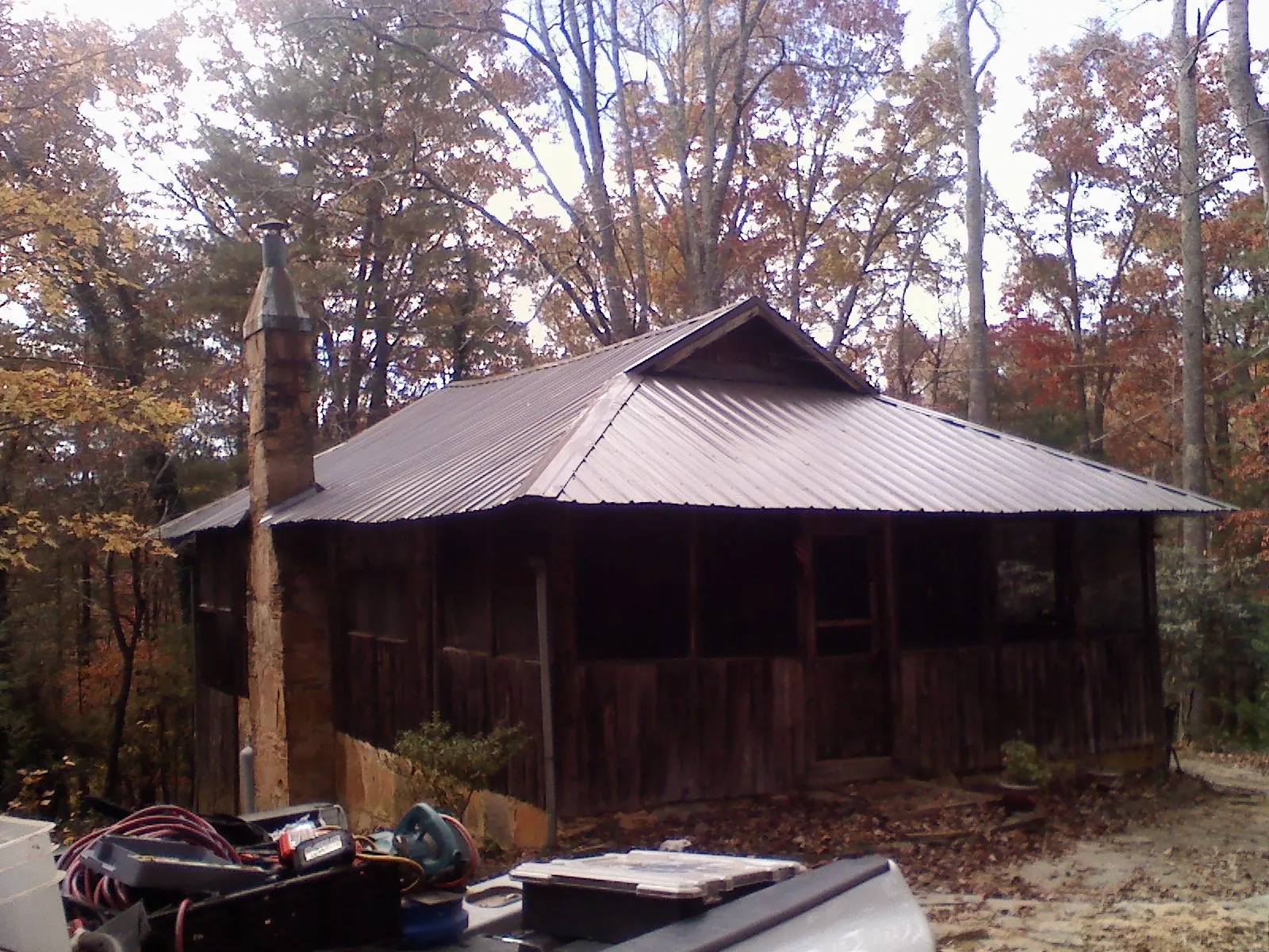 Brown metal hip roof on an old cabin with a stone chimney in Athol