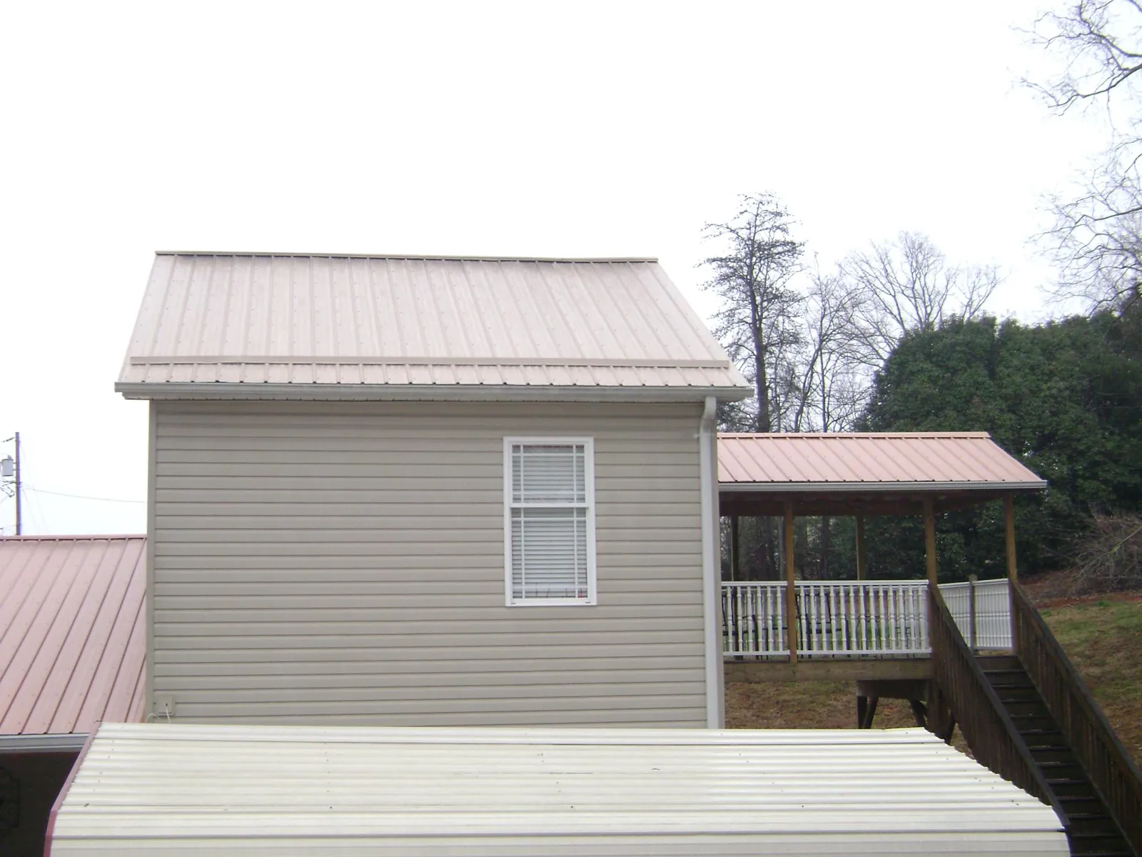 Tan metal roofs on a two story addition and attached porch, from a Roof Replacement job in Athol